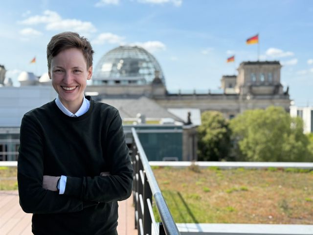 Foto von Rebecca Lenhard. Sie steht lächelnd vor dem Reichstagsgebäude.